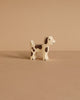 A Holztiger Small Farm Dog, a handcrafted white wooden figurine with brown spots, stands on a beige surface against a matching background, highlighting its high-quality artistry.