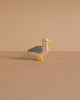 The Holztiger Seagull is a small, handcrafted wooden figurine featuring gray wings, a white head, yellow beak and feet. It stands on a plain beige surface with a matching background. Made in Europe by HOLZTIGER.