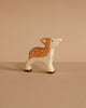 The Holztiger Fawn, a small handcrafted wooden deer with brown and white painted details, stands on a beige surface against a matching beige background.