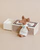 A small Maileg Big Sister Mouse in Box toy dressed in a white dress with blue accents, standing beside an open white gift box on a beige background.