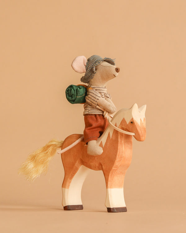 The Maileg Big Brother Horseback Adventure Set features a hiker mouse with a hat, shirt, and backpack sitting on a handmade wooden horse against a plain beige background.