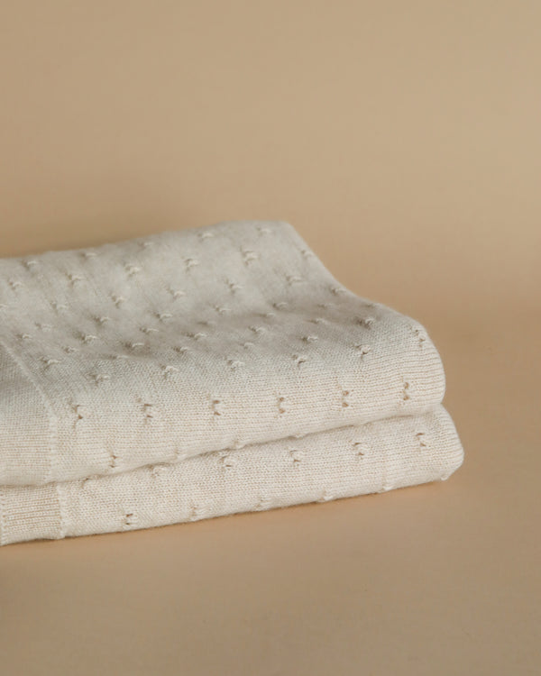 A neatly folded white towel with a textured, dotted pattern, placed on a Handmade Merino Wool Bibi Blanket - Cream background.