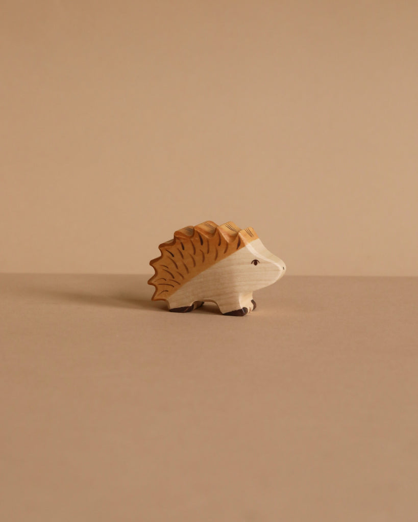 A small, handcrafted Holztiger Hedgehog wood figurine with natural tones rests on a beige surface and background, evoking the charm of European-made HOLZTIGER figures.