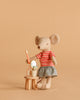 The Maileg Big Sister Getting Ready Set features a mouse in a red striped shirt and skirt with a toothbrush, standing by a wooden stool with a mirror, cup, and toiletries—creating an adorable scene against a light brown background.