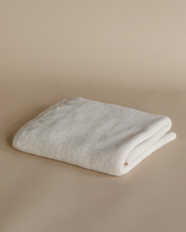 A neatly folded white towel placed on a Handmade Merino Wool Felix Blanket - Cream.