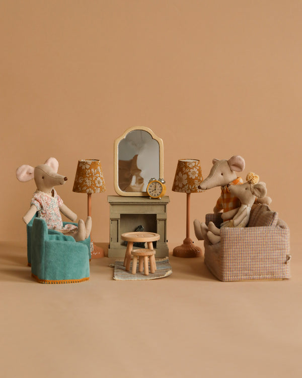 The Maileg Living Room Set features stuffed mice in a cozy, beige setting with fabric armchairs, a stool, fireplace, mirror, vintage-style lamps, and a small mantel clock.