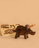 A Handmade Wooden Paleo Triceratops Dinosaur stands assembled in the foreground on a beige surface, while an animal-shaped wooden puzzle is visible in the background.