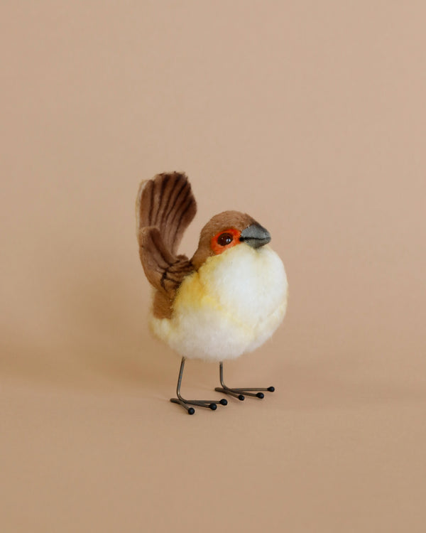 A handmade Wren Bird Stuffed Animal with a white and brown body, orange eye detail, and black metal feet, positioned against a soft peach background. This piece is part of our collection of hand-sewn animals.