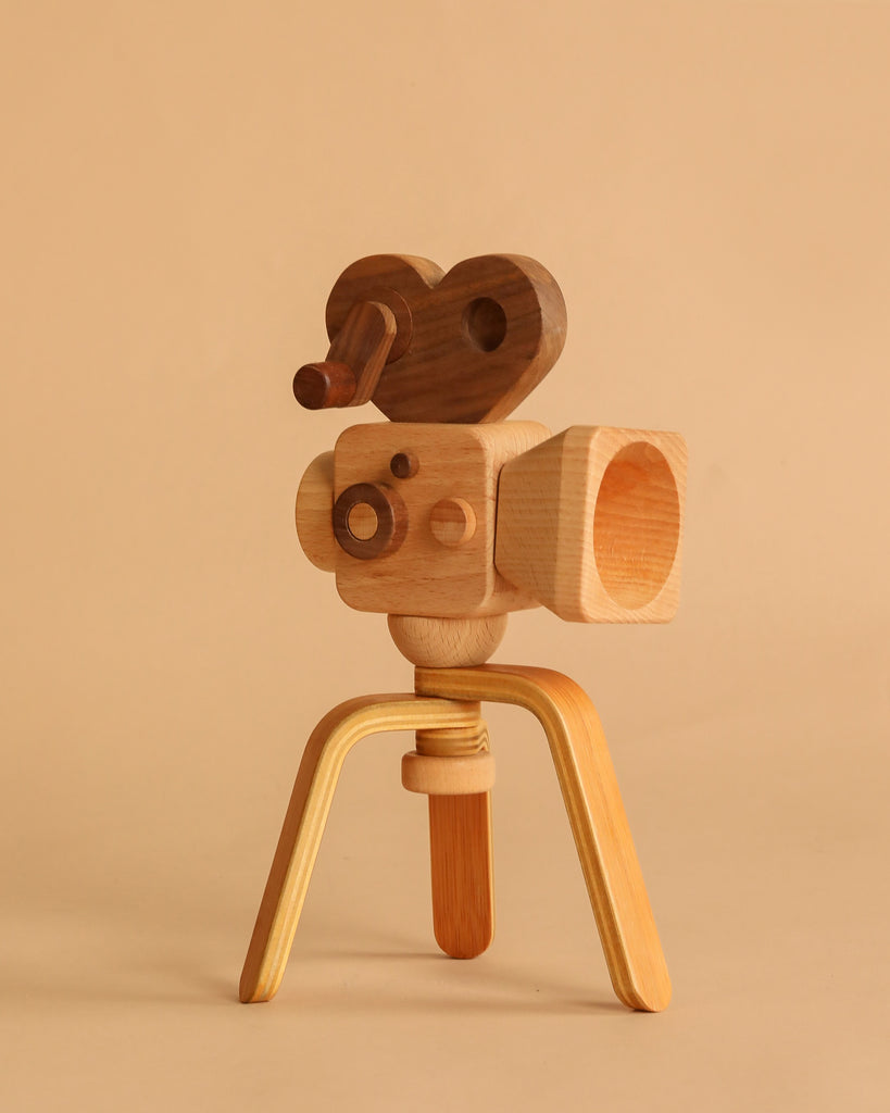 The Father’s Factory | Super 16 Pro Wooden Toy Camera with Tripod features a heart-shaped handle and three-legged stand, perfect for storytelling and pretend play—all showcased against a beige background.