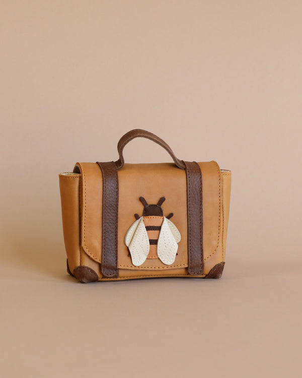 A stylish tan Donsje Trychel Bum Bag - Bee with dark brown adjustable leather straps and an adorable white and brown bee-shaped keychain attached to the front, set against a soft beige background.