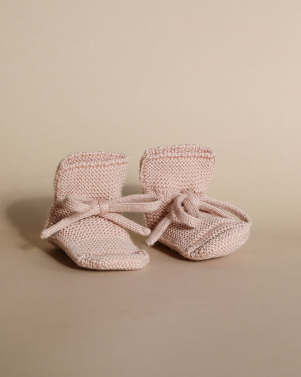A pair of Handmade Merino Wool Booties - Apricot with bows, displayed on a beige background.