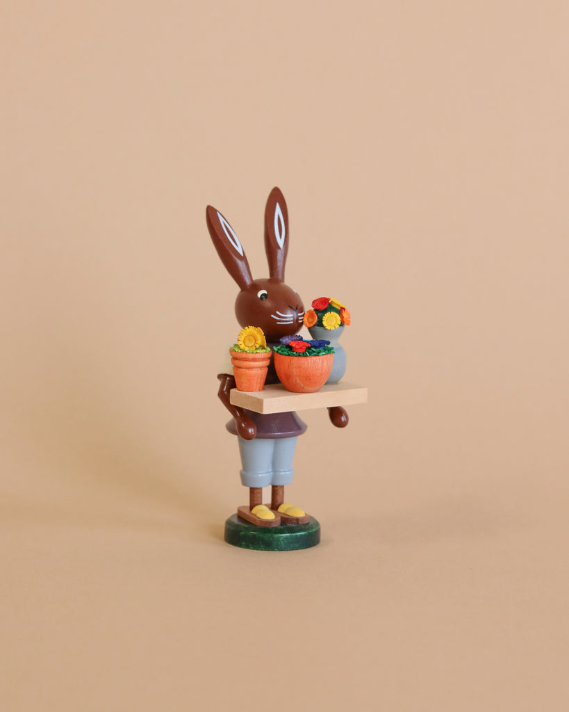 A cherished Collectible Dregeno Easter Figure - Bunny Florist in overalls holding a wheelbarrow filled with colorful flowers against a soft beige background.