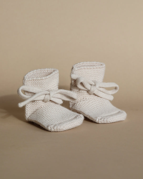 A pair of Handmade Merino Wool Booties in Cream, featuring lace-up details, displayed against a soft beige background.