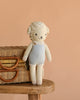 The Easter Basket Set features a hand knit lamb doll with curly wool, blue overalls, and a gentle expression, standing beside a handmade basket on a wooden stool against a beige background.