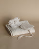 A neatly folded baby blanket with tiny embroidered details accompanied by a pair of small white baby booties and a Handmade Merino Wool Newborn Bonnet - Cream, all set against a soft beige background.