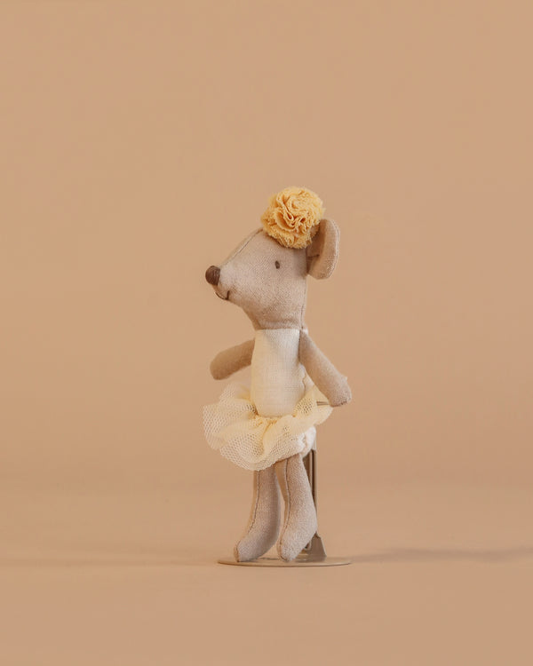 The Maileg Ballerina Mouse, Little Sister - Off White, is a small gray mouse in a cream tutu with a yellow flower headband, standing upright against a plain beige background.
