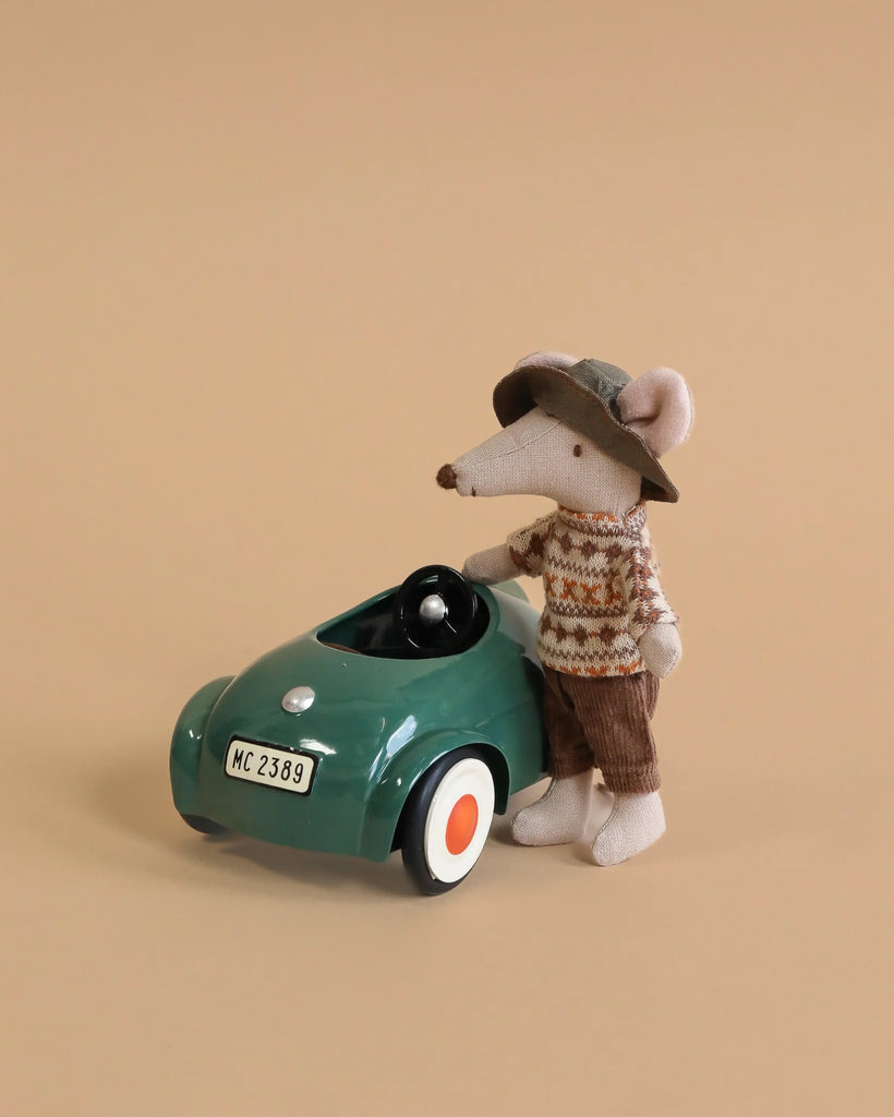 The Maileg Big Brother Mouse Holiday Adventure Set features a mouse in a sweater, brown pants, and hat beside a green car with "MC 2389" license plate and cute accessories, ready for adventure on a beige background.