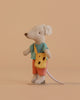 A Maileg Little Brother Adventure Set mouse, dressed in a blue striped shirt, orange shorts, and carrying a yellow cheese-shaped bag, stands on a neutral beige background. This charming Adventure Set mouse is perfect for imaginative play and storytelling.