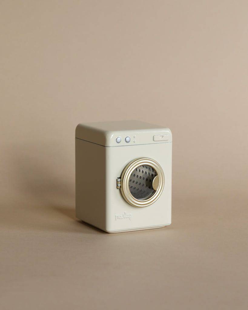 The Maileg Laundry Room Set features a small, beige washing machine with a front-loading door and simple top buttons, displayed on a matching surface against a light beige background.