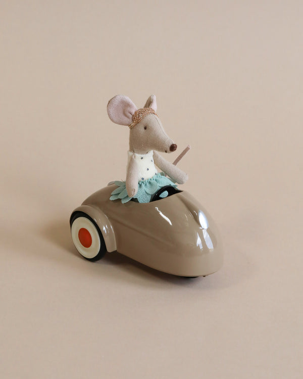 A small plush Maileg Mouse Car - Light Brown dressed in a turquoise outfit, sitting and steering a miniature metal vintage car, set against a light beige background.