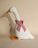 A Maileg Large Goose doll decorated with a pink bow tie around its neck, standing against a soft beige background.
