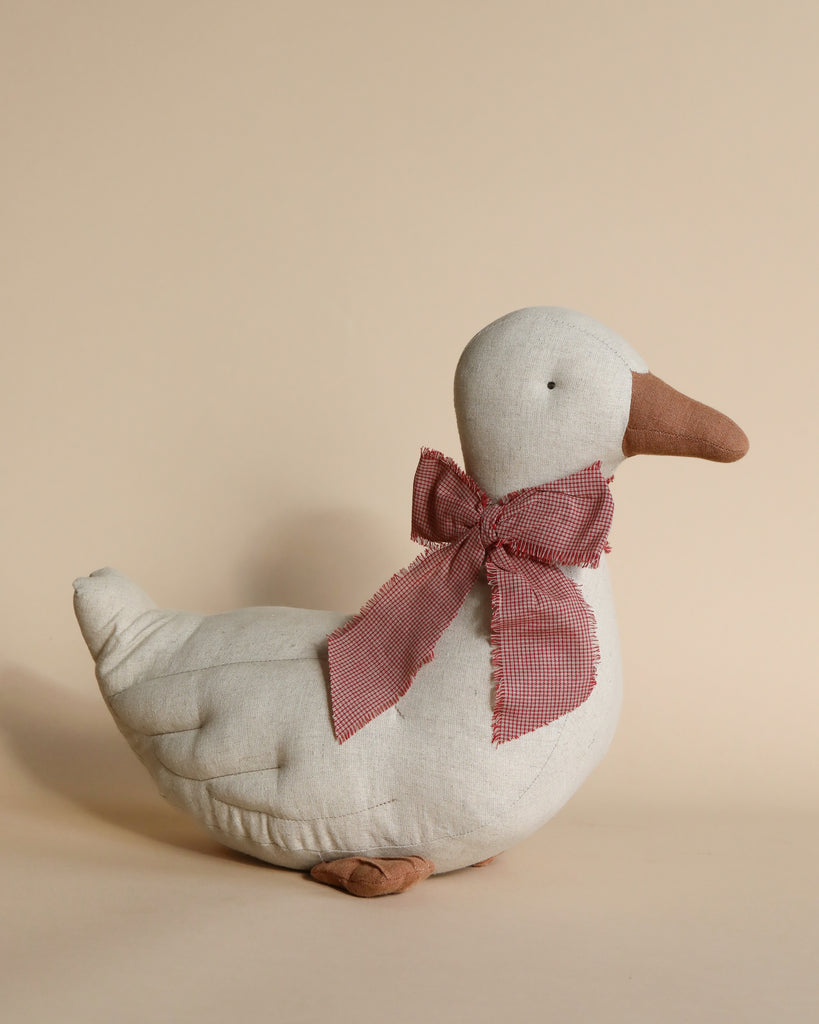 A Maileg Duck - Sand with a checkered pink bow tied around its neck, displayed against a plain beige background. The duck is white with a brown beak and feet, perfect as festive décor.
