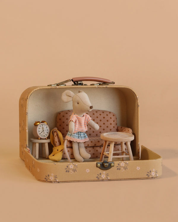 The Maileg Little Sister Mini House Set features a mouse in a pink shirt and blue skirt with a sofa bed, table, chair, clock, and toy cheese set inside an open Maileg suitcase on a beige background.