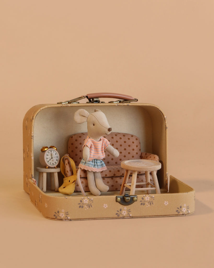 The Maileg Little Sister Mini House Set features a mouse in a pink shirt and blue skirt with a sofa bed, table, chair, clock, and toy cheese set inside an open Maileg suitcase on a beige background.