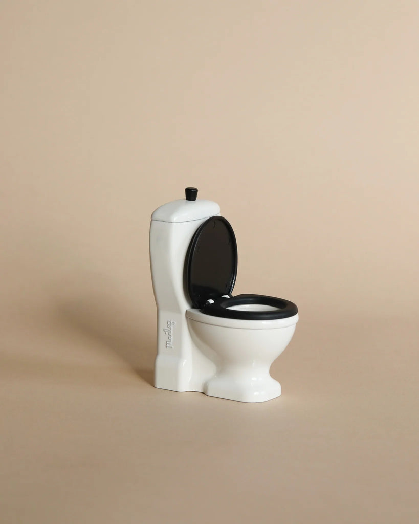 A small, white Maileg Bathroom Set toy with a black seat and open lid sits against a beige background—a charming accessory for the Maileg Wellness Accessories collection.