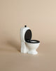 Mini white toilet with back lid. Photographed against beige background. 