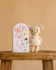 Cuddle + Kind Tiny Emma the Mouse, a hand-knit doll in a pink dress, stands on a wooden bench beside a pastel floral box featuring a mouse illustration, handmade in Peru and set against a plain beige background.