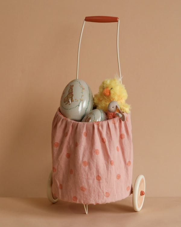 The Easter Trolley Set includes a stylish vintage-style cart with a pale pink linen/cotton basket adorned with orange dots, pastel-colored oval tins, and a fluffy yellow chick toy. The white metal frame features two wheels and a brown handle, perfect for showcasing soft toys like the Maileg Micro Bunny.