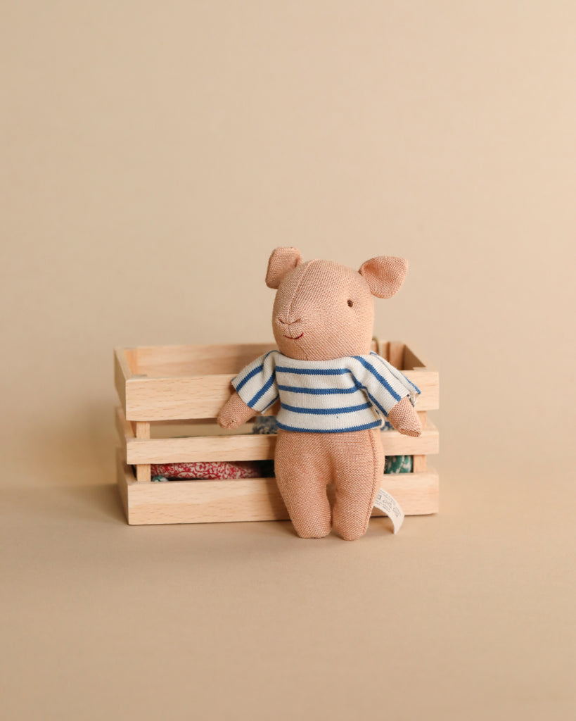 A small Maileg Pig In Box, Baby - Boy toy wearing a striped shirt, sitting in a miniature wooden box against a plain beige background.
