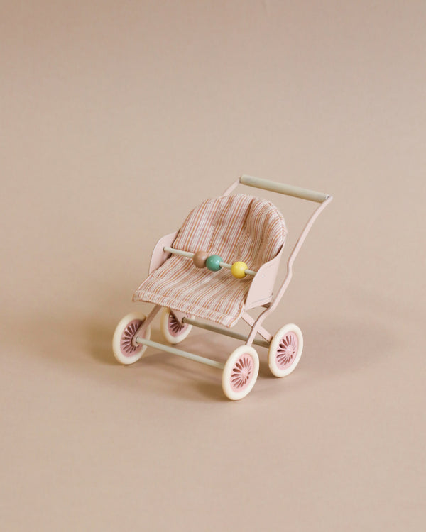A Maileg stroller, baby mice - rose with a striped fabric seat contains three colorful Easter eggs, set against a plain light beige background.