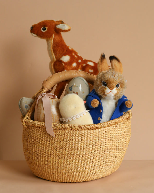 The Large Easter Basket Set includes a wicker basket with a plush rabbit in a blue jacket, a toy chick, and a soft stuffed fawn, each featuring realistic details. A neutral beige background enhances their handcrafted charm.