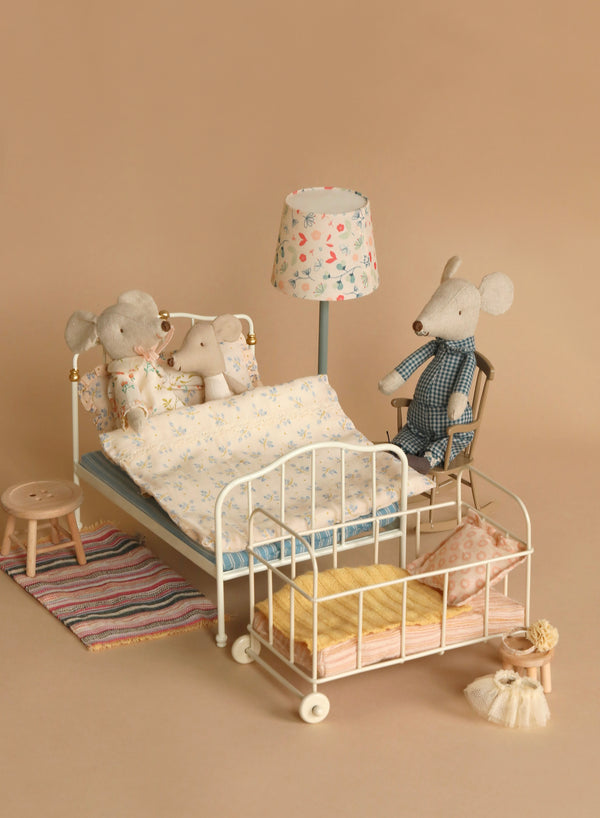 A charming Maileg Set - Sleepover At Grandparents features a small metal-framed doll bed with a white finish and elegant gold accents on the headboard. This delightful set includes a blue mattress dressed with a cream-colored blanket adorned with floral patterns and a matching pillow, perfect for Grandparents Mice to enjoy imaginative play.