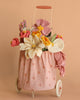 The Basket of Felt Flowers features a colorful felt flower arrangement with white, yellow, and pink blooms in a small trolley basket with a pink polka-dot fabric bag, displayed on a matching peach background.