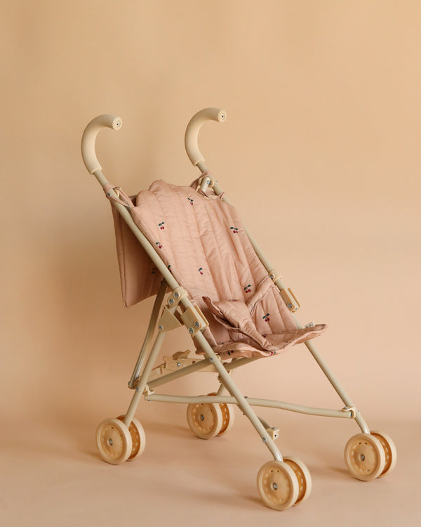 A Konges Sløjd doll stroller in cherry with a quilted fabric seat and beige double wheels, set against a soft beige background.