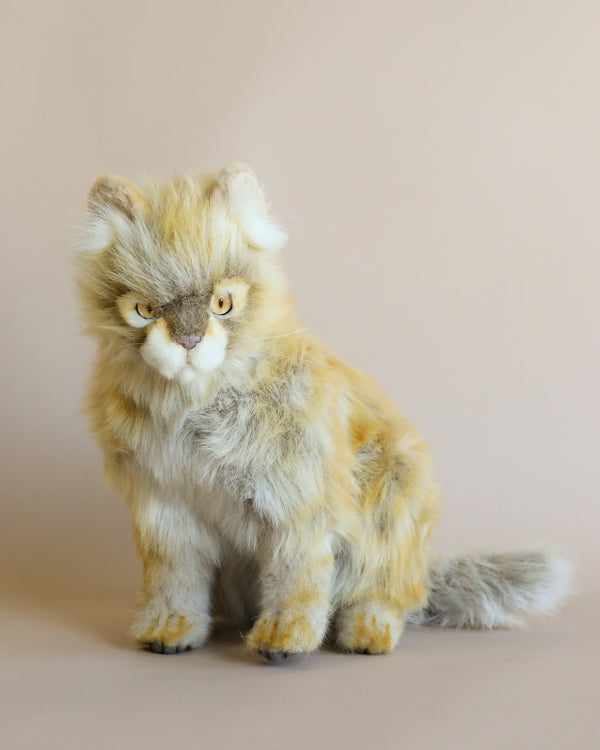 A Tan Calico Cat stuffed animal with a fluffy yellow and white coat and piercing amber eyes, sitting against a plain light beige background.