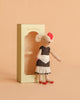 The Maileg Beautician Mouse, Mum wears a black dress, white apron, red shoes, and a red flower headpiece. She stands beside a beige "Beautician" box, ready to inspire endless imaginative dress-up play.
