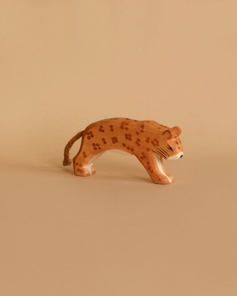 The Ostheimer Leopard is a small, handcrafted wooden figure that features painted spots and is depicted in a walking pose against a beige background. Reminiscent of Ostheimer's style, this figure boasts a simple, minimalist design that emphasizes the natural wood texture and muted colors, making it perfect for imaginative play.