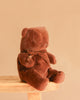 A Maileg Teddy Bear in Carry Cot sits on a wooden stool against a plain beige background.