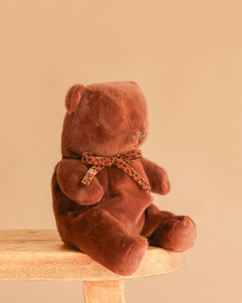 A Maileg Teddy Bear in Carry Cot sits on a wooden stool against a plain beige background.