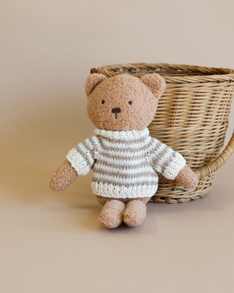 Sentence with product name: A small, plush Teddy Bear in a polyester cotton white and gray striped sweater, sitting in front of a woven basket on a light beige background.