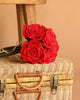 The Handcrafted Felt Flower Bouquet rests on a wicker suitcase, with a wooden stool and a beige background behind them.
