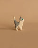 Ostheimer Gray and White Cat, Head Up: A small wooden figurine painted gray with white legs and a white face. The cat has a single green eye, an upright tail, and stands on a plain beige background. Its simple and minimalist design is reminiscent of Ostheimer toys handcrafted from sustainably sourced materials.