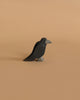 The Ostheimer Raven, a small and simplistic black bird figurine with a white beak and feet, stands against a plain beige background. This handcrafted wooden toy boasts a minimalist and artisan appearance, reminiscent of the beloved Ostheimer toys, and is crafted from sustainably sourced materials.