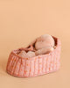 A Maileg Sleeping Bunny in Carry Cot rests in a quilted, pink floral-patterned bed against a soft peach background.