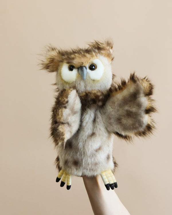A person holds a Owl Puppet, with big eyes and fluffy feathers, extended on a hand against a soft beige background. The puppet is realistic with detailed wings and talons from the HANSA animals.