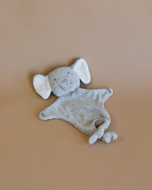 A small, well-worn Elephant Lovey plush toy with floppy ears and a content smile, lying on a plain peach background. This charming piece is handmade from organic cotton.